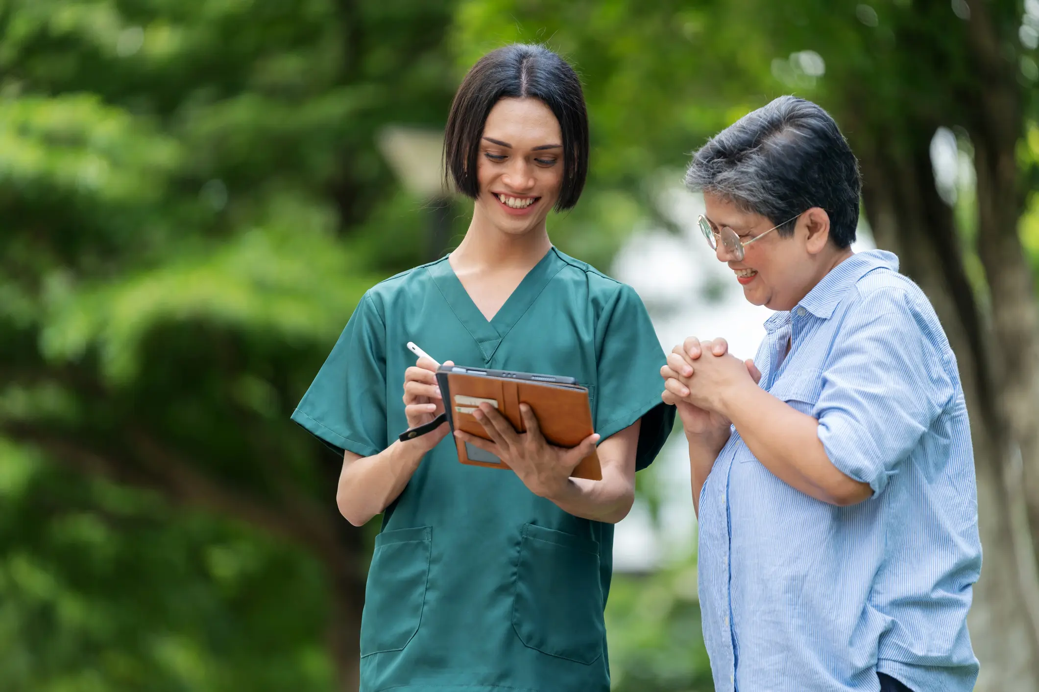 Nurse showing tablet to elderly woman outdoors.