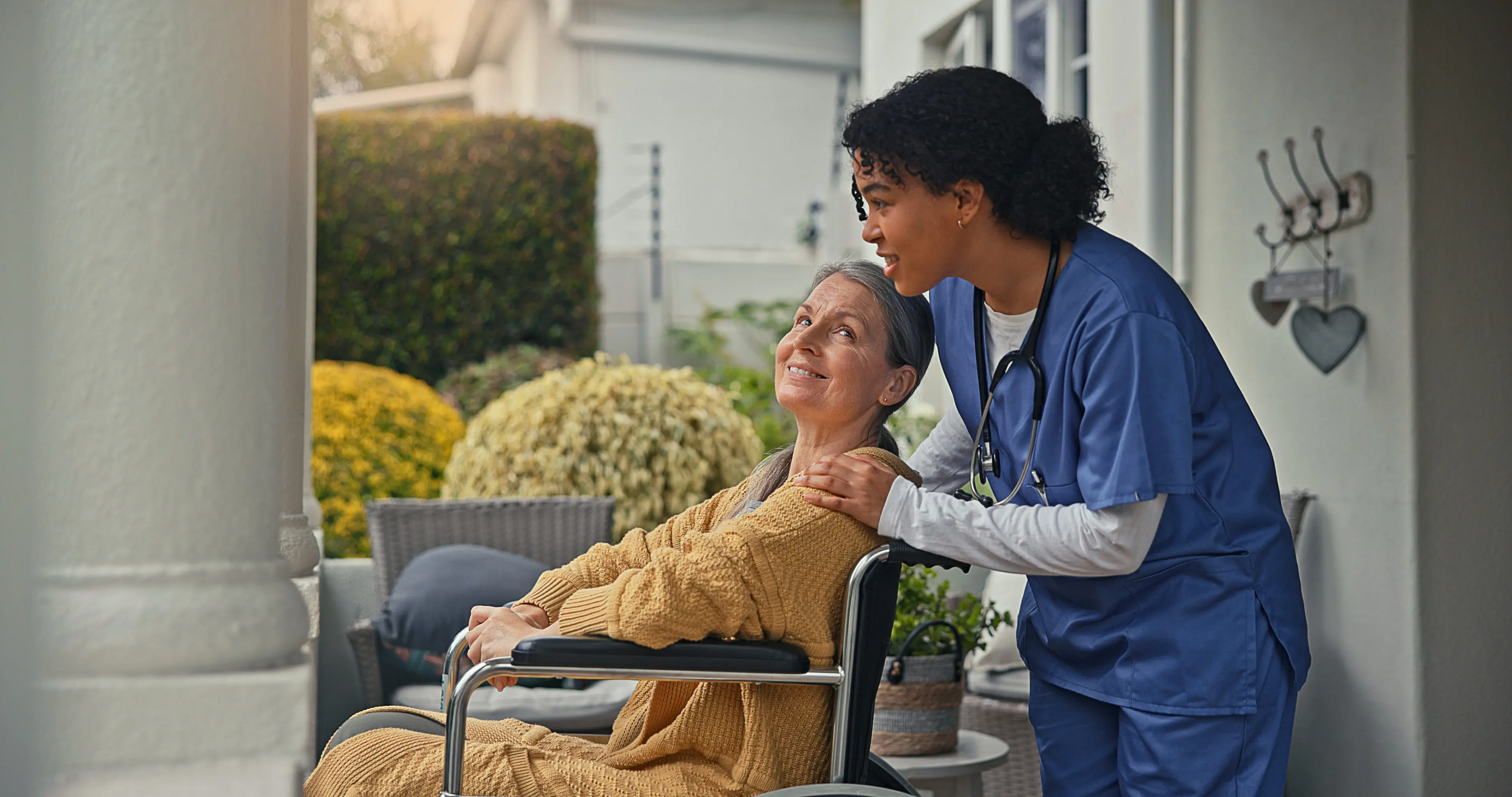 A nurse gently supporting an elderly woman in a wheelchair outdoors.