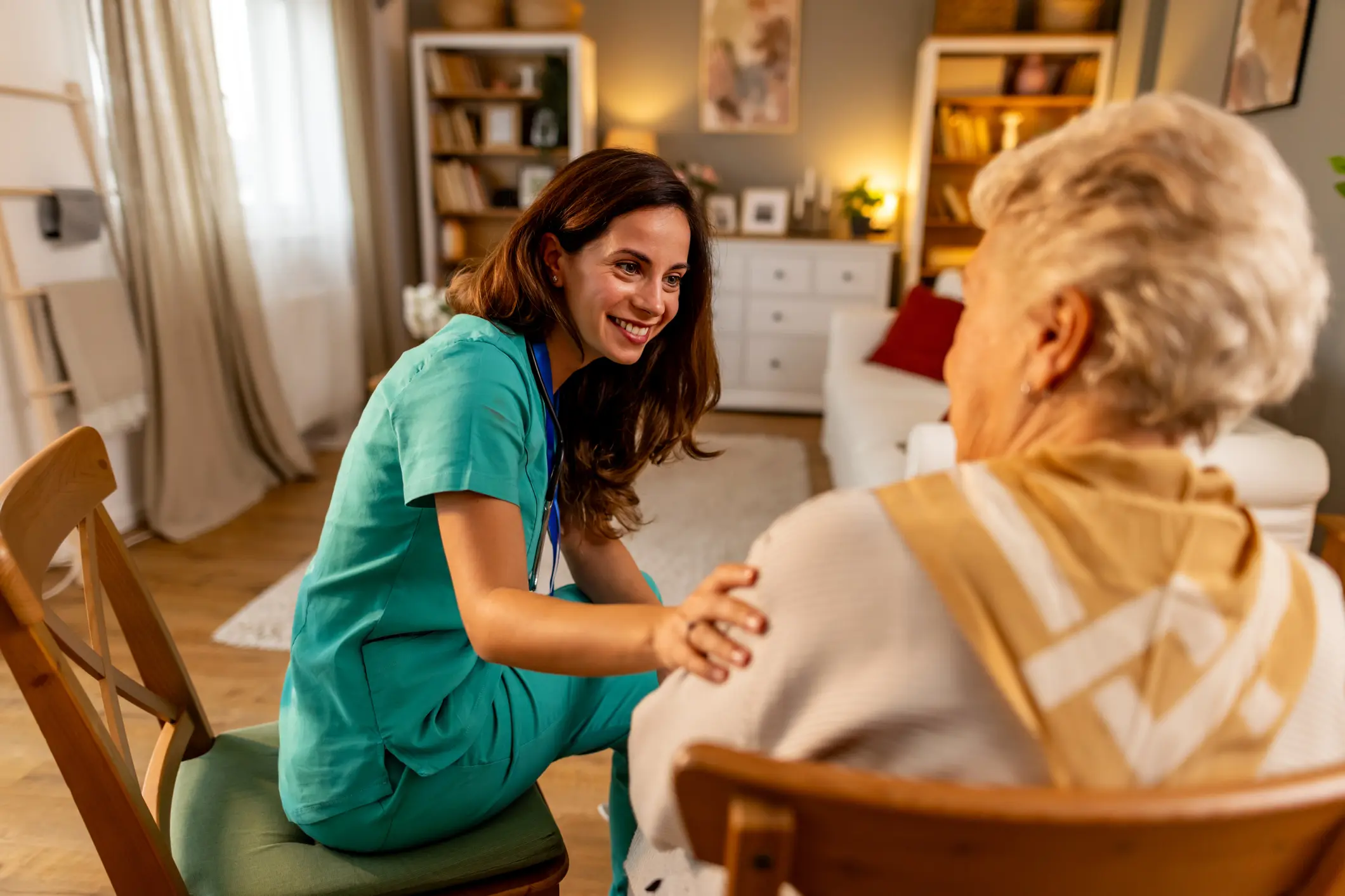 A caregiver chats warmly with an elderly woman in a cozy living room.