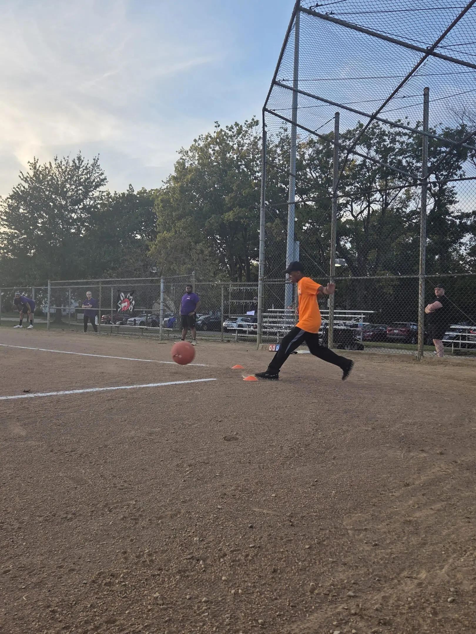 Child in orange shirt playing baseball, running on dirt field.