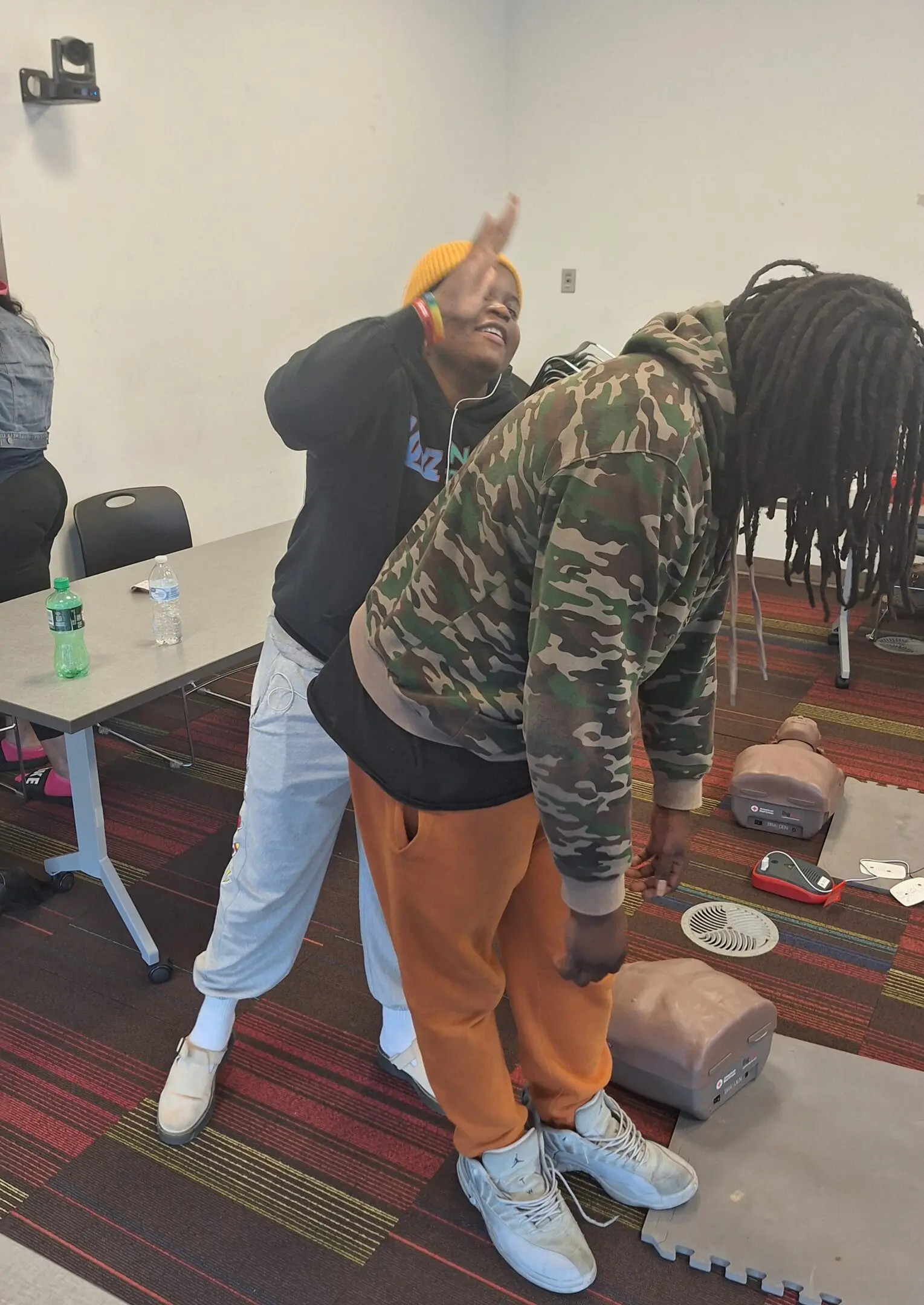 Two people in a casual room, one playfully posing behind the other.